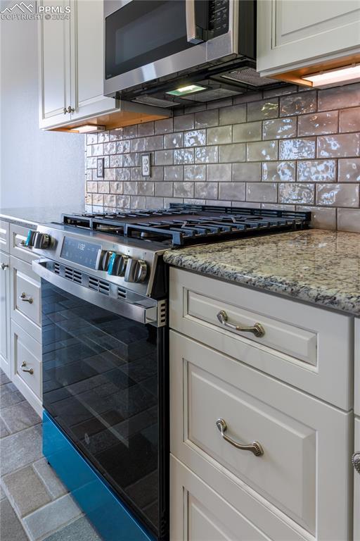 kitchen with backsplash, light stone counters, white cabinetry, and stainless steel appliances