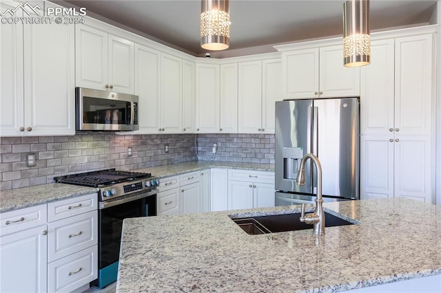 kitchen featuring appliances with stainless steel finishes, backsplash, sink, white cabinets, and hanging light fixtures