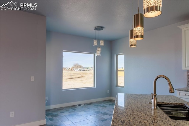 kitchen with light stone countertops, decorative light fixtures, white cabinetry, and sink