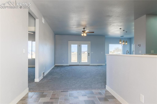 unfurnished living room with a wealth of natural light, ceiling fan with notable chandelier, and dark colored carpet