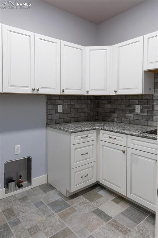 kitchen with tasteful backsplash, dark stone countertops, and white cabinetry