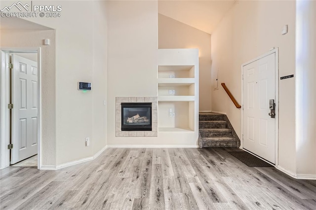 unfurnished living room featuring built in shelves, a tile fireplace, lofted ceiling, and light wood-type flooring