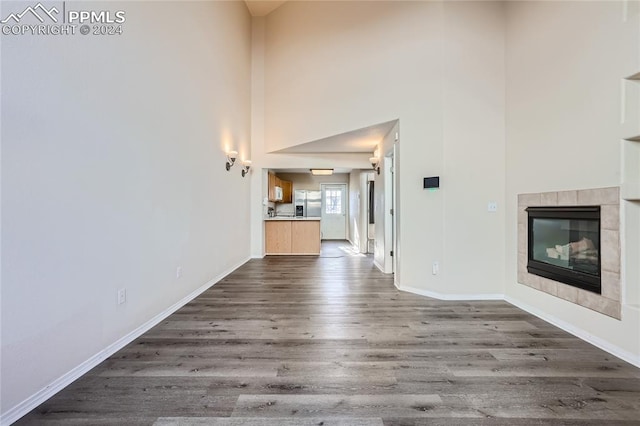 unfurnished living room with hardwood / wood-style floors, a towering ceiling, and a tiled fireplace