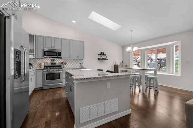 kitchen featuring a center island, vaulted ceiling with skylight, decorative backsplash, decorative light fixtures, and stainless steel appliances