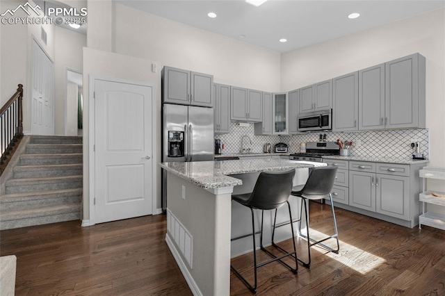 kitchen featuring a towering ceiling, appliances with stainless steel finishes, a kitchen island, light stone counters, and a breakfast bar area