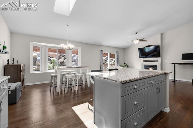 kitchen featuring gray cabinetry, a center island, ceiling fan with notable chandelier, hanging light fixtures, and a breakfast bar area