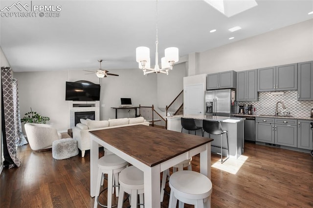 dining area featuring lofted ceiling, sink, dark wood-type flooring, and ceiling fan with notable chandelier