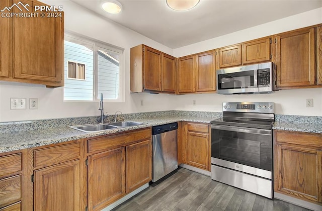 kitchen with dark hardwood / wood-style floors, light stone counters, sink, and appliances with stainless steel finishes