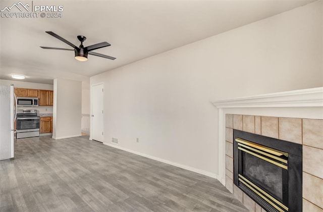 unfurnished living room with ceiling fan, light wood-type flooring, and a tile fireplace