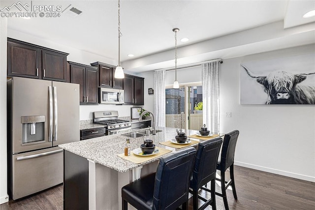 kitchen featuring stainless steel appliances, sink, decorative light fixtures, a breakfast bar area, and an island with sink