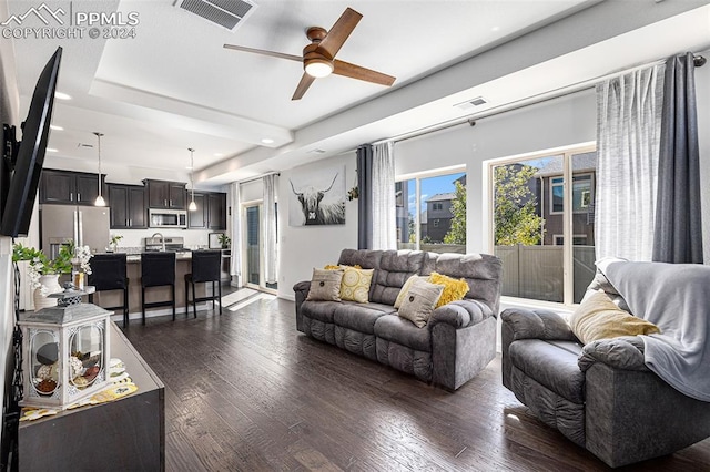 living room with a tray ceiling, ceiling fan, and dark hardwood / wood-style floors