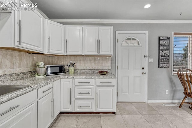 kitchen with white cabinets, backsplash, light stone counters, and crown molding