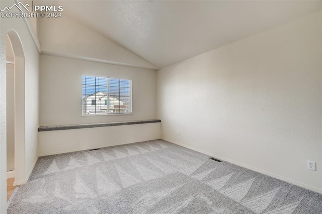 spare room featuring lofted ceiling and light carpet