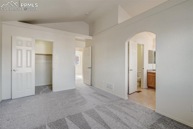 unfurnished bedroom with ensuite bath, light carpet, and lofted ceiling