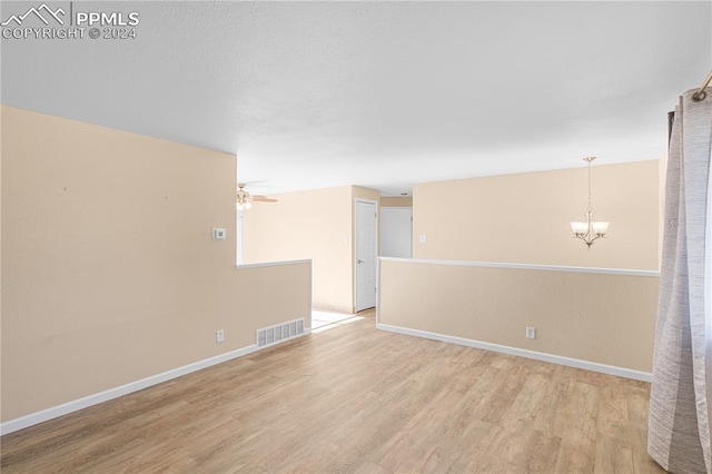 spare room featuring ceiling fan with notable chandelier and light hardwood / wood-style flooring