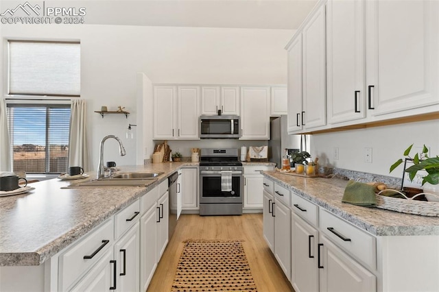 kitchen with sink, white cabinets, light hardwood / wood-style floors, stainless steel appliances, and a center island with sink