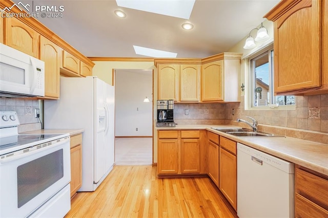 kitchen featuring a skylight, light wood finished floors, light countertops, a sink, and white appliances