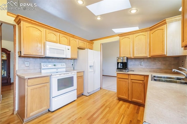 kitchen with a skylight, light wood finished floors, light countertops, a sink, and white appliances