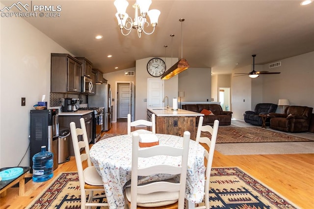 dining space with hardwood / wood-style floors, ceiling fan with notable chandelier, sink, and vaulted ceiling