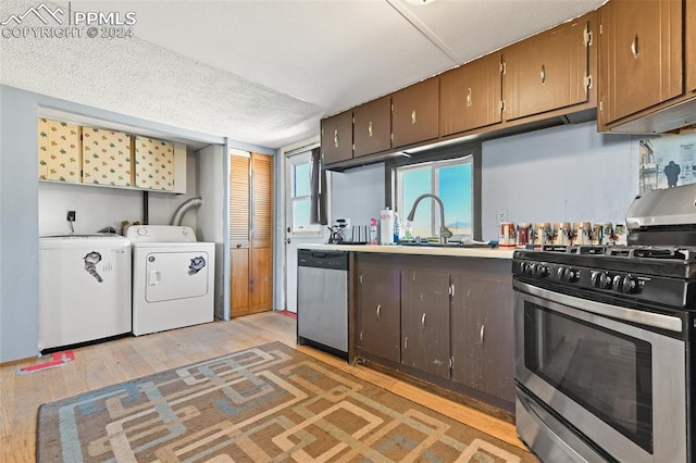 kitchen with appliances with stainless steel finishes, a textured ceiling, sink, washing machine and clothes dryer, and light hardwood / wood-style floors