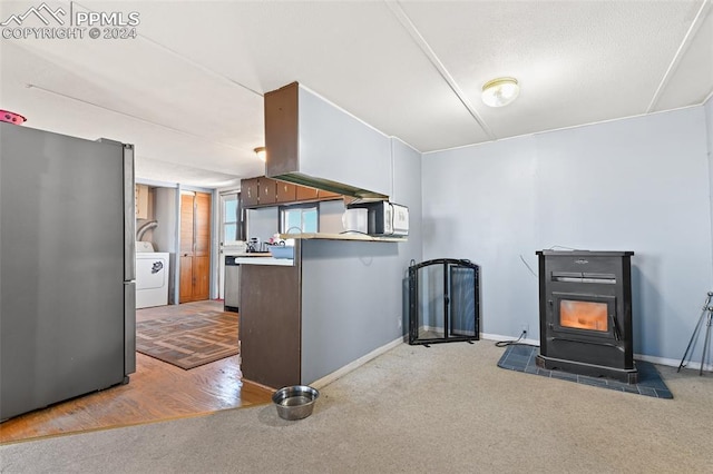 kitchen with a wood stove, stainless steel fridge, light colored carpet, kitchen peninsula, and washer / dryer