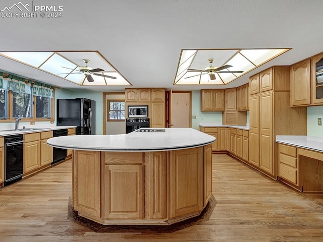 kitchen with black appliances, light hardwood / wood-style floors, sink, and an island with sink