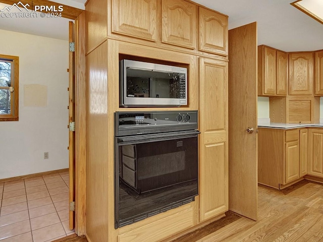 kitchen featuring light brown cabinetry, light wood-type flooring, black oven, and stainless steel microwave