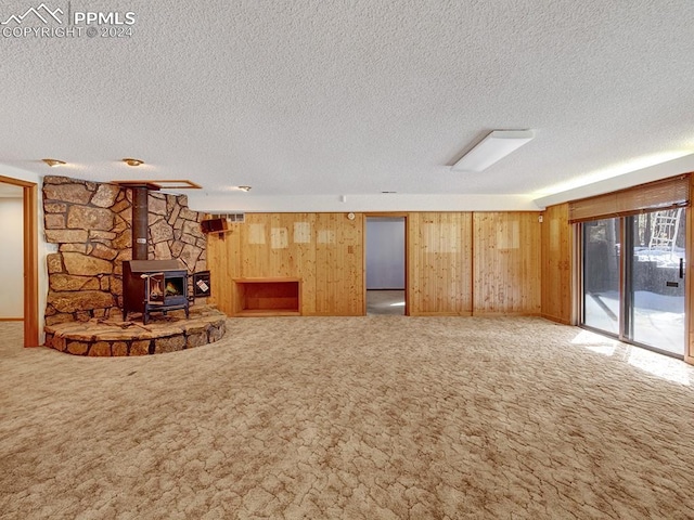 unfurnished living room featuring a textured ceiling, wood walls, a wood stove, and carpet floors