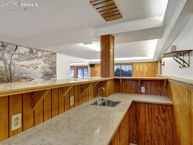 kitchen featuring a textured ceiling, sink, and wooden walls