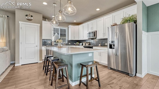 kitchen featuring white cabinets, light hardwood / wood-style floors, appliances with stainless steel finishes, decorative light fixtures, and a kitchen island