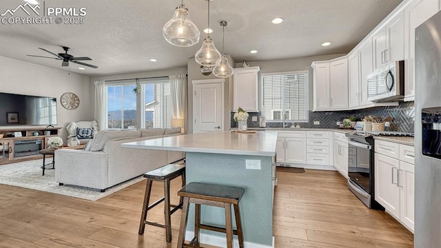 kitchen with ceiling fan, white cabinets, a breakfast bar, a kitchen island, and appliances with stainless steel finishes