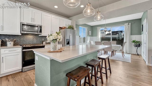 kitchen featuring a center island, white cabinets, stainless steel appliances, and decorative light fixtures