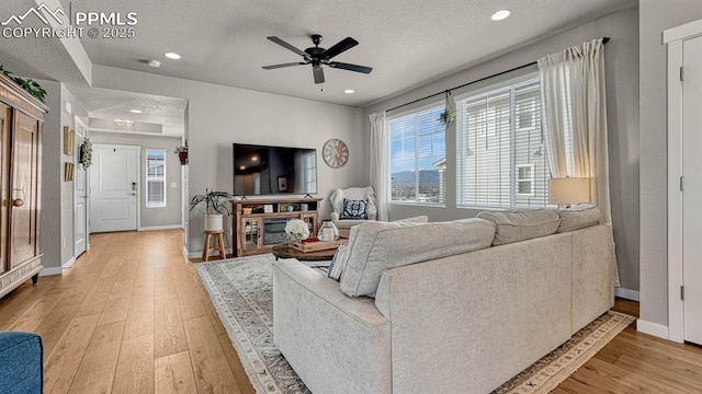 living room featuring ceiling fan, a textured ceiling, and light wood-type flooring