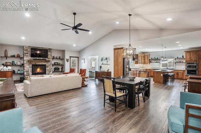 dining room featuring high vaulted ceiling, a stone fireplace, dark hardwood / wood-style floors, ceiling fan, and a wealth of natural light