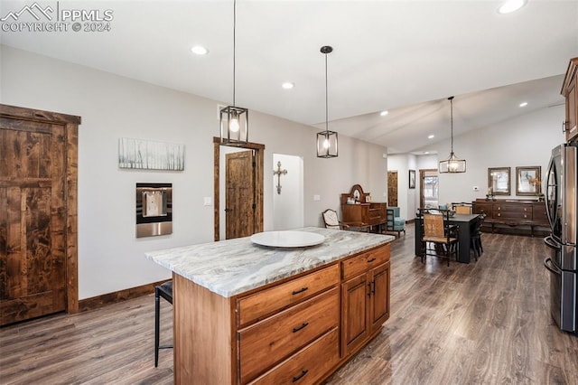 kitchen featuring light stone countertops, dark hardwood / wood-style flooring, decorative light fixtures, a kitchen island, and stainless steel refrigerator