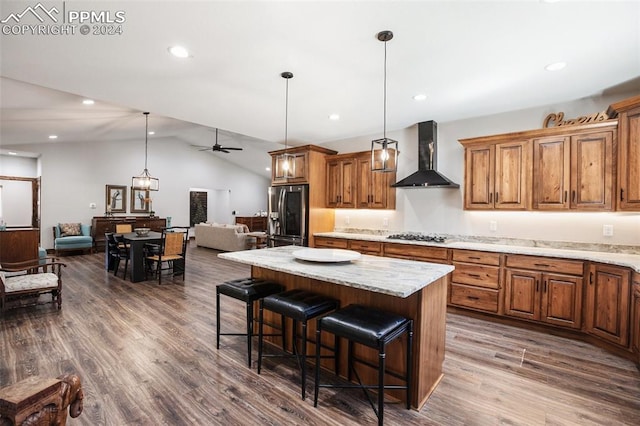 kitchen featuring ceiling fan, a center island, wall chimney exhaust hood, vaulted ceiling, and appliances with stainless steel finishes