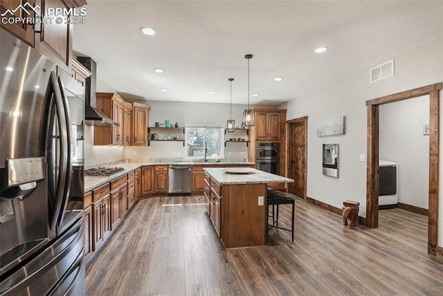 kitchen featuring wall chimney exhaust hood, a kitchen breakfast bar, pendant lighting, a kitchen island, and appliances with stainless steel finishes