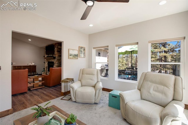 living area with a stone fireplace, ceiling fan, and dark hardwood / wood-style flooring