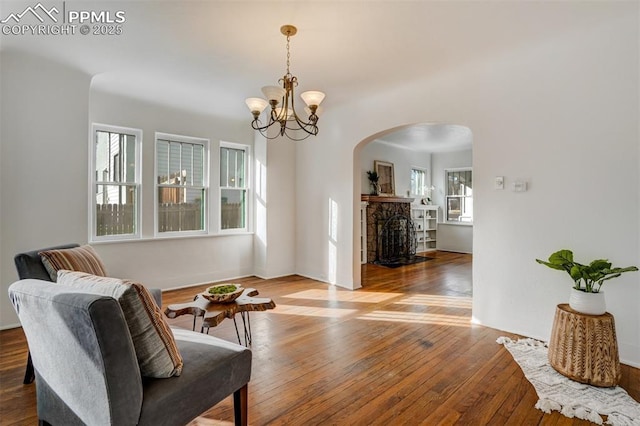 sitting room featuring hardwood / wood-style flooring, a stone fireplace, and an inviting chandelier