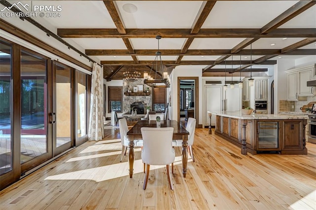 dining area featuring coffered ceiling, a stone fireplace, light hardwood / wood-style flooring, beam ceiling, and beverage cooler