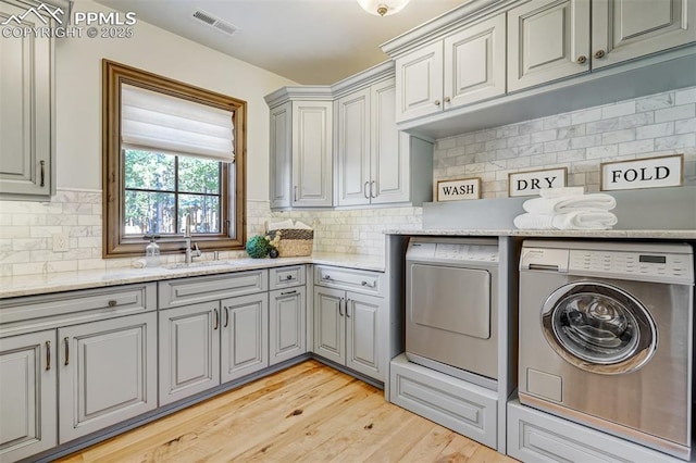 clothes washing area with washer and clothes dryer, cabinets, light wood-type flooring, and sink