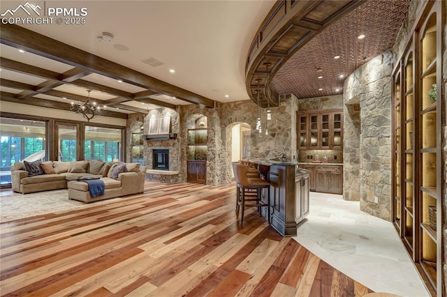 interior space with beam ceiling, light stone counters, a fireplace, and a chandelier