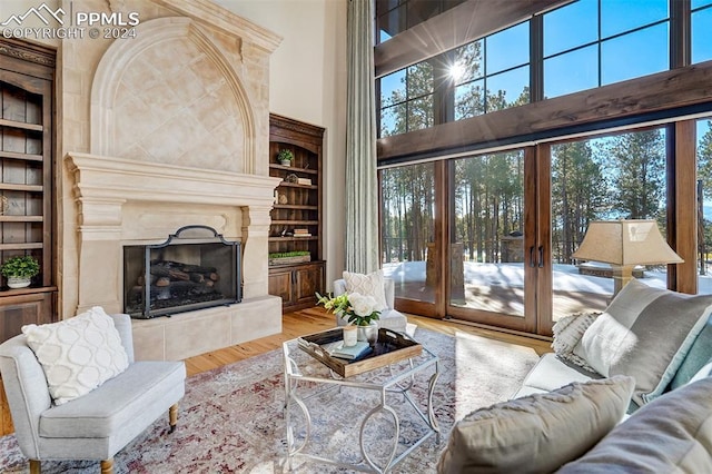 living room featuring french doors, light wood-type flooring, built in features, a fireplace, and a high ceiling