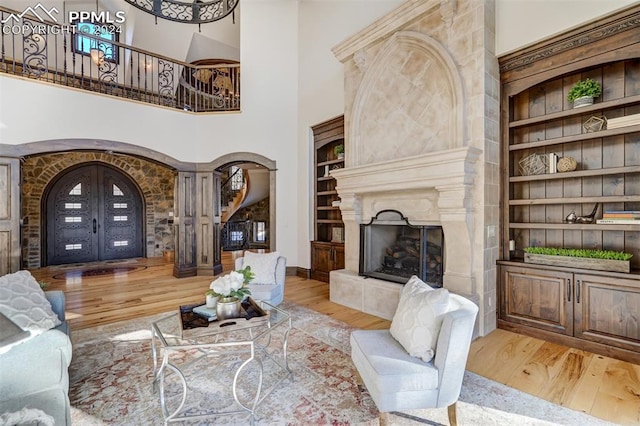 living room with a fireplace, built in shelves, light hardwood / wood-style flooring, and a high ceiling