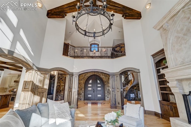 living room featuring french doors, a high ceiling, beamed ceiling, decorative columns, and light wood-type flooring