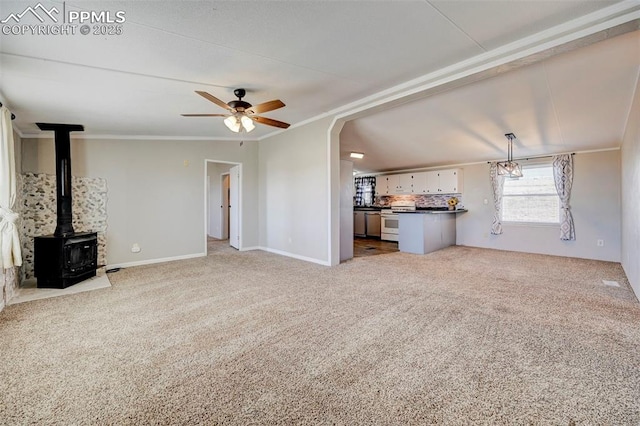 unfurnished living room with light carpet, a wood stove, ceiling fan, and ornamental molding