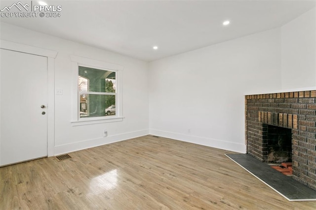 unfurnished living room featuring light hardwood / wood-style floors and a brick fireplace