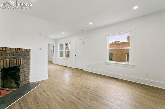 unfurnished living room with light hardwood / wood-style floors and a brick fireplace