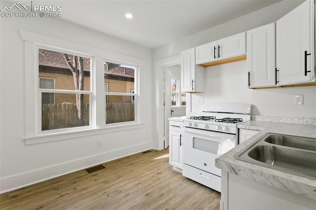 kitchen with white cabinets, light wood-type flooring, white range with gas cooktop, and sink