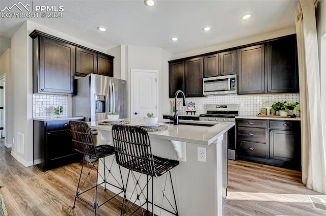 kitchen with dark brown cabinetry, an island with sink, light hardwood / wood-style floors, a breakfast bar, and appliances with stainless steel finishes